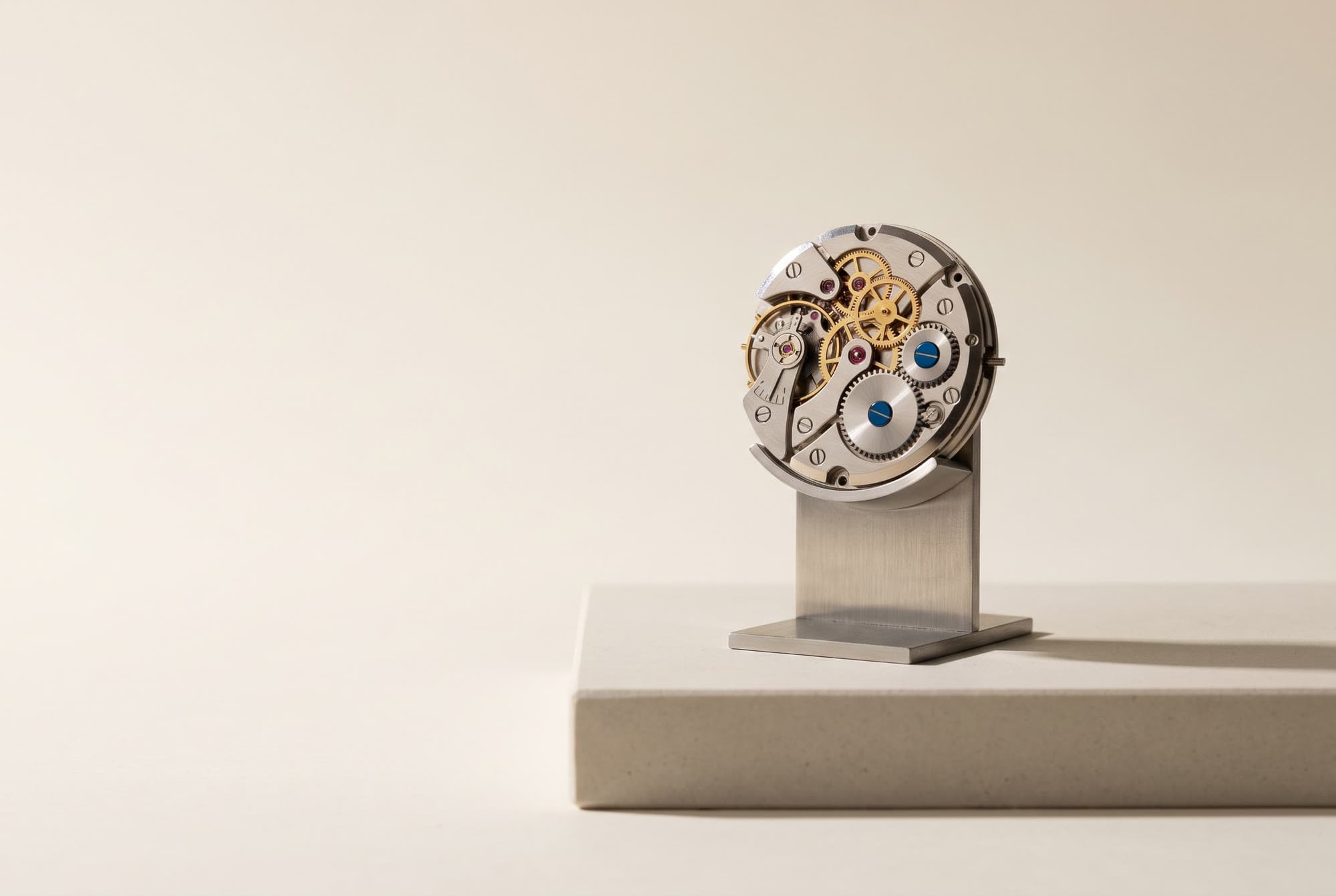 An exposed mechanical watch movement on a steel stand, two cobalt screws among the gears